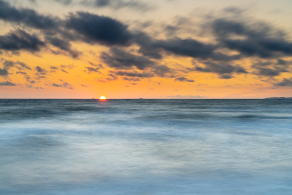 o sol está se pondo sobre o oceano com nuvens no céu