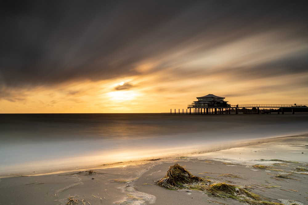 the sun is setting over the ocean with a pier in the background