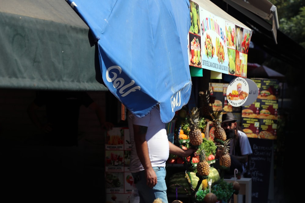 青いTシャツと白い短パンを着た女性が果物屋の前に立つ