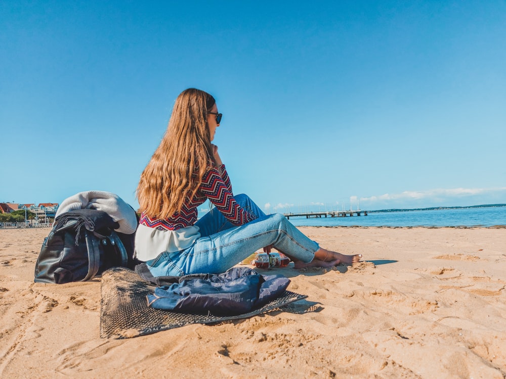 woman in blue denim jeans sitting on brown sand during daytime