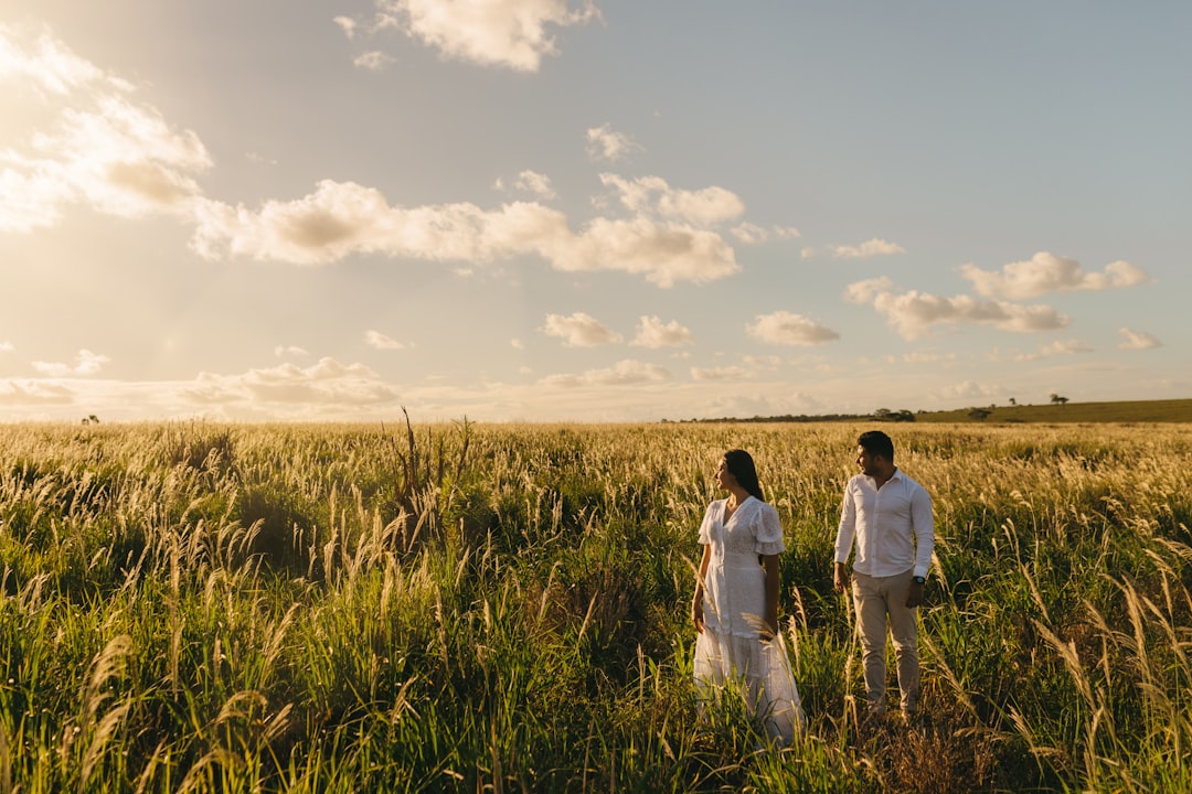 man and woman walking on green grass field under white clouds during daytime