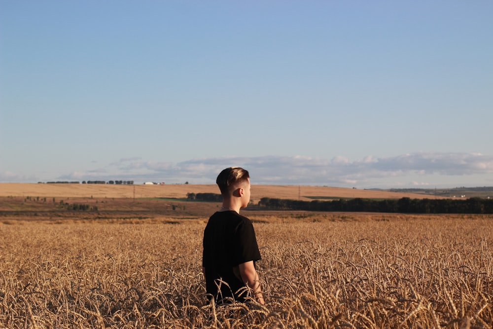 homme en noir ras du cou T-shirt assis sur le terrain d’herbe brune pendant la journée