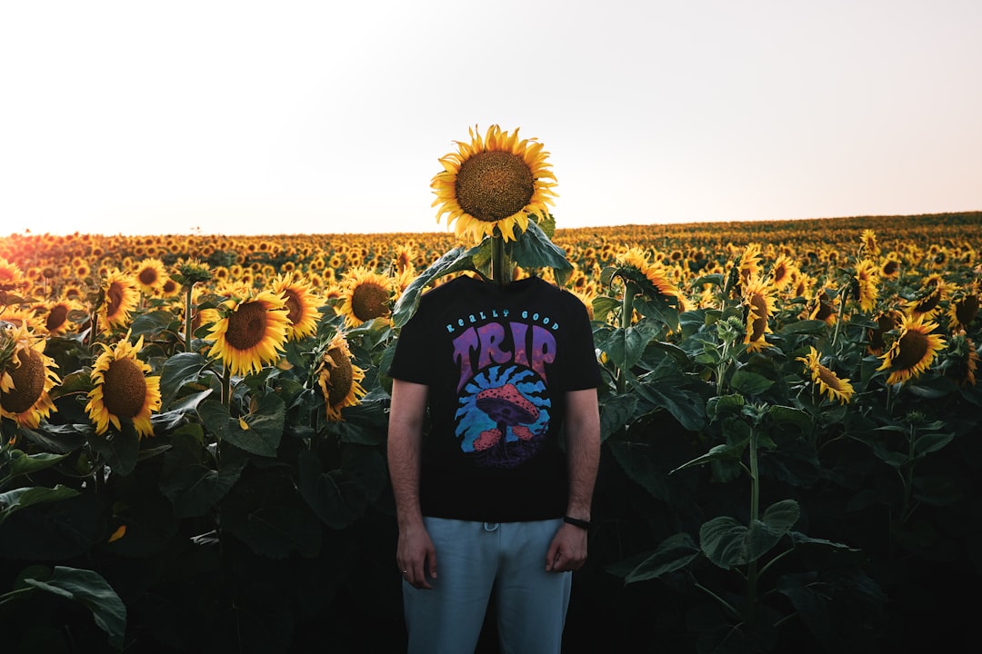 man in black crew neck t-shirt standing on sunflower field during daytime