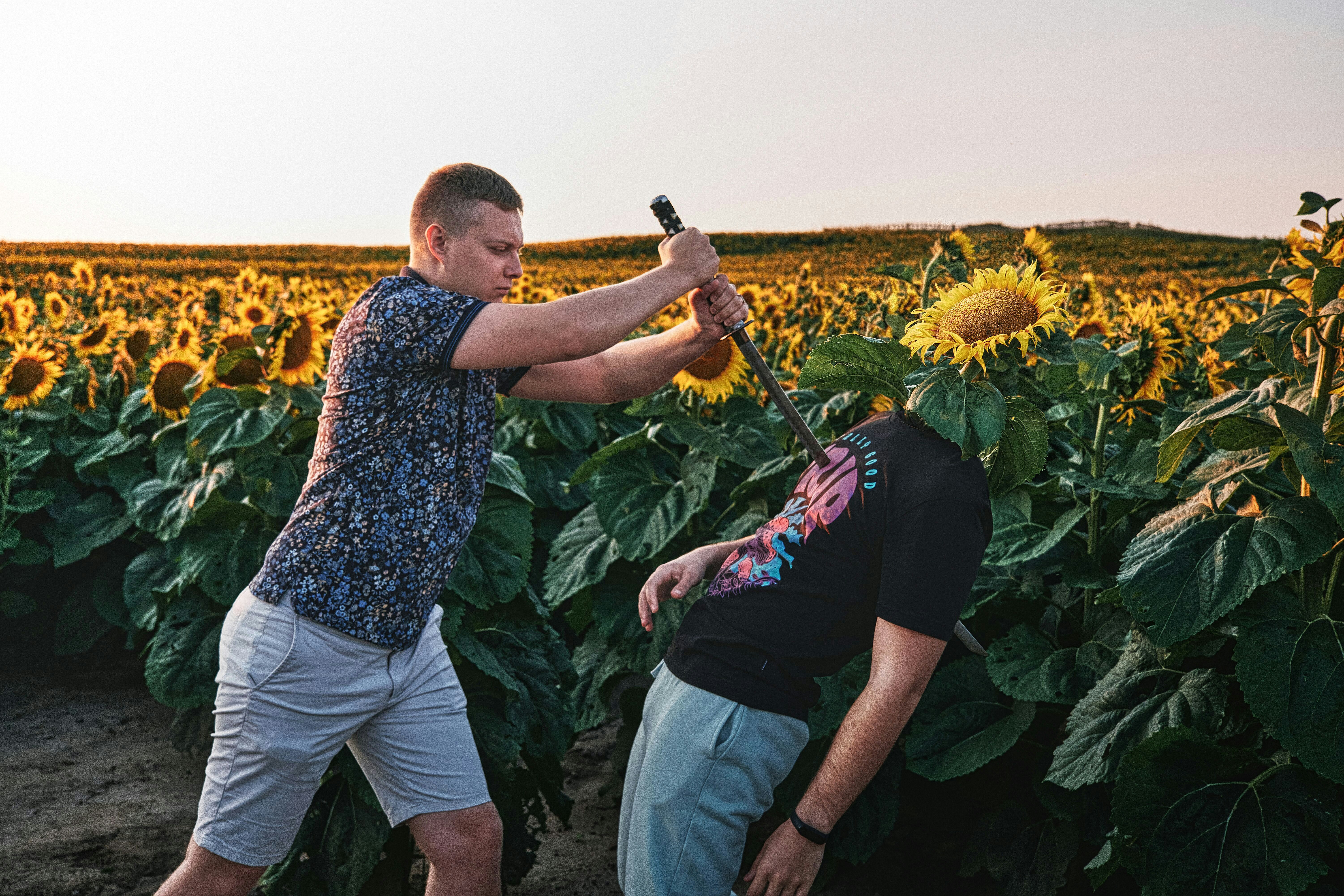 man in black t-shirt and gray shorts holding black stick standing beside yellow sunflower field