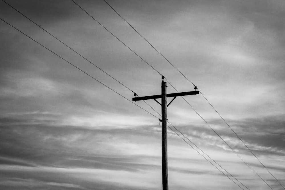 grayscale photo of electric post under cloudy sky