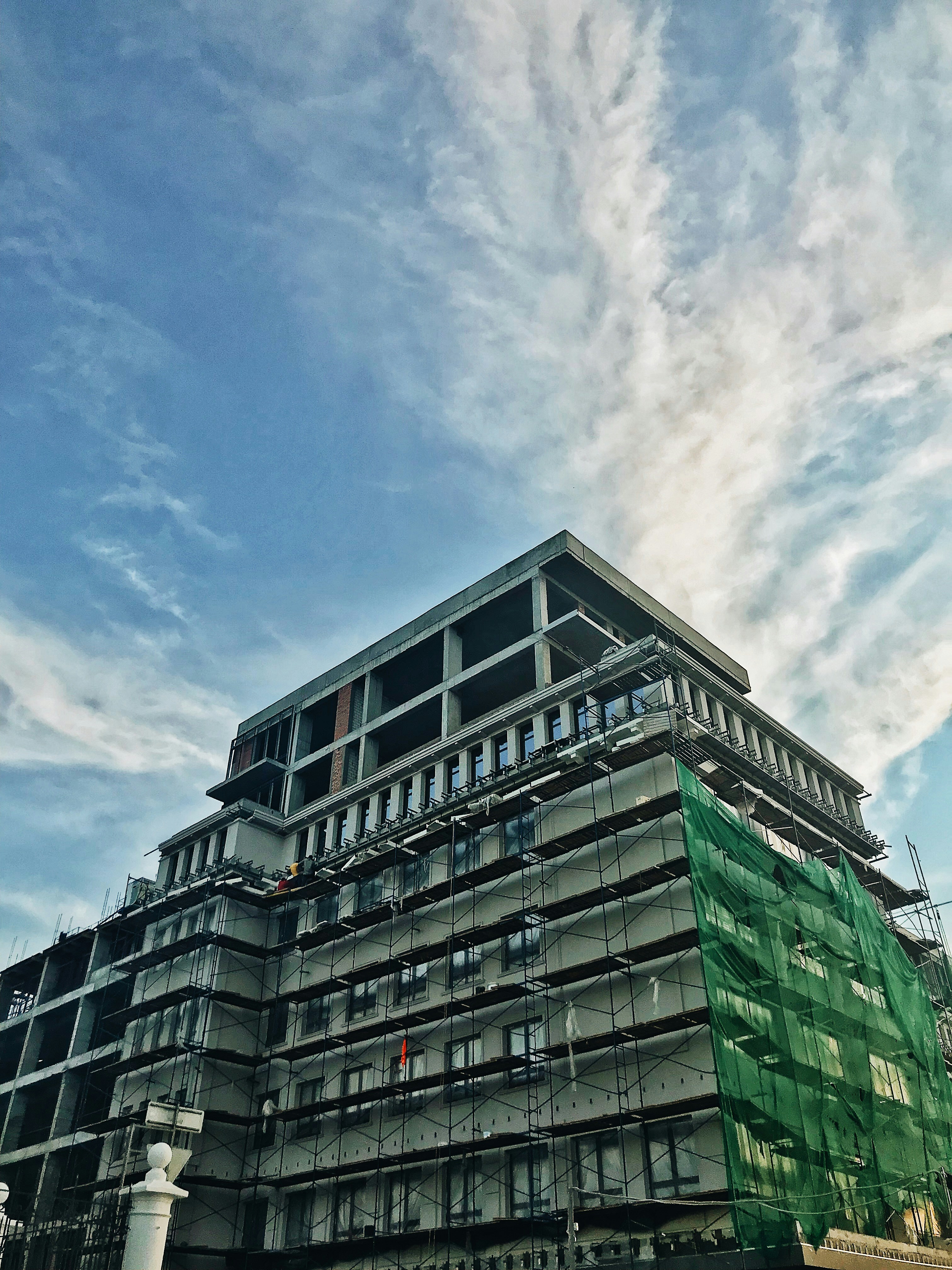 Multi-storey commercial building under construction with scaffolding, workers in hard hats, overcast sky