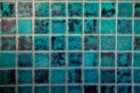 A grid of square tiles with a teal and dark blue marbled effect, creating a textured and vibrant pattern. Each tile has a unique combination of shades, contributing to an overall mosaic appearance.