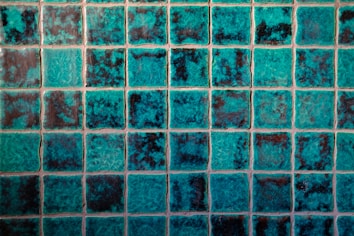 A grid of square tiles with a teal and dark blue marbled effect, creating a textured and vibrant pattern. Each tile has a unique combination of shades, contributing to an overall mosaic appearance.