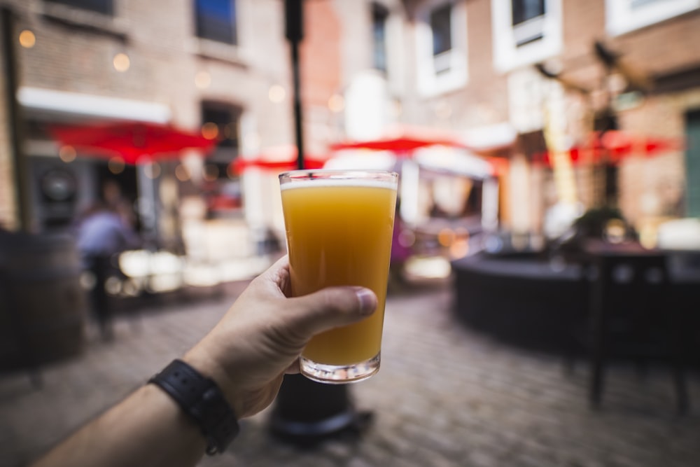 personne tenant un verre à boire transparent avec un liquide brun