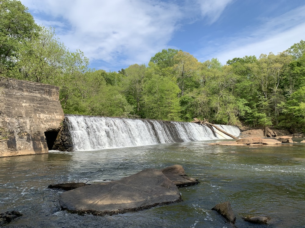 waterfalls near green trees under blue sky during daytime