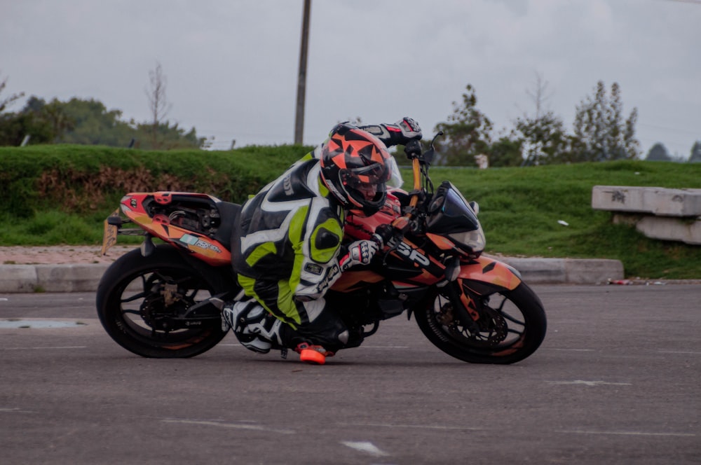 man in green and black motorcycle suit riding on orange sports bike