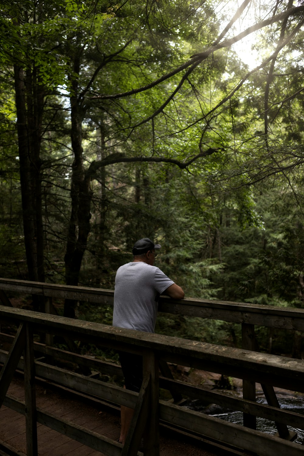 man in white shirt sitting on brown wooden bridge