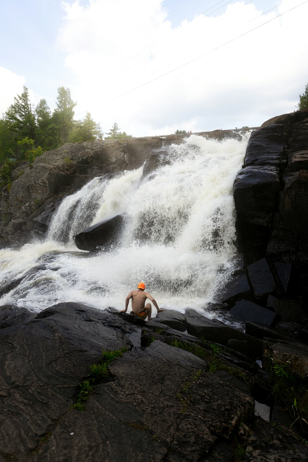 woman in yellow tank top sitting on rock near waterfalls during daytime