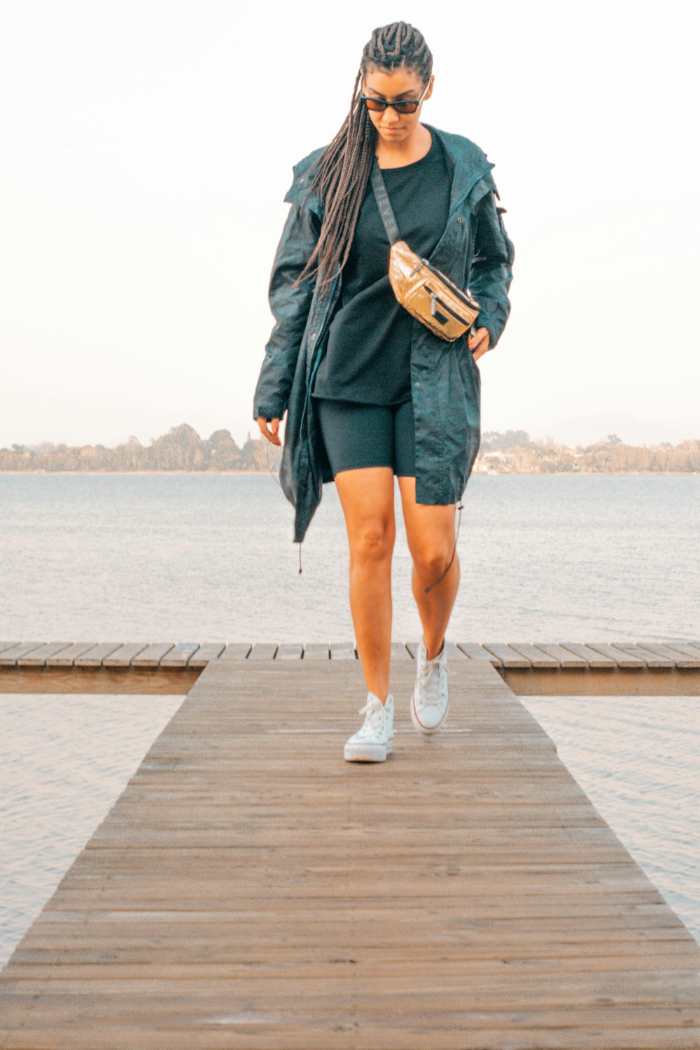 woman in black leather jacket and blue denim shorts standing on wooden dock during daytime