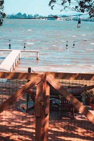 A wide shot of a serene lakeside venue with draped fabric and fairy lights ready for a wedding celebration.