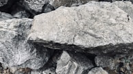 A collection of large gray stones with rough, textured surfaces and irregular shapes. The stones appear stacked or scattered, creating a natural and rugged composition.