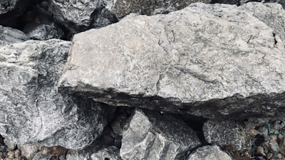 A collection of large gray stones with rough, textured surfaces and irregular shapes. The stones appear stacked or scattered, creating a natural and rugged composition.