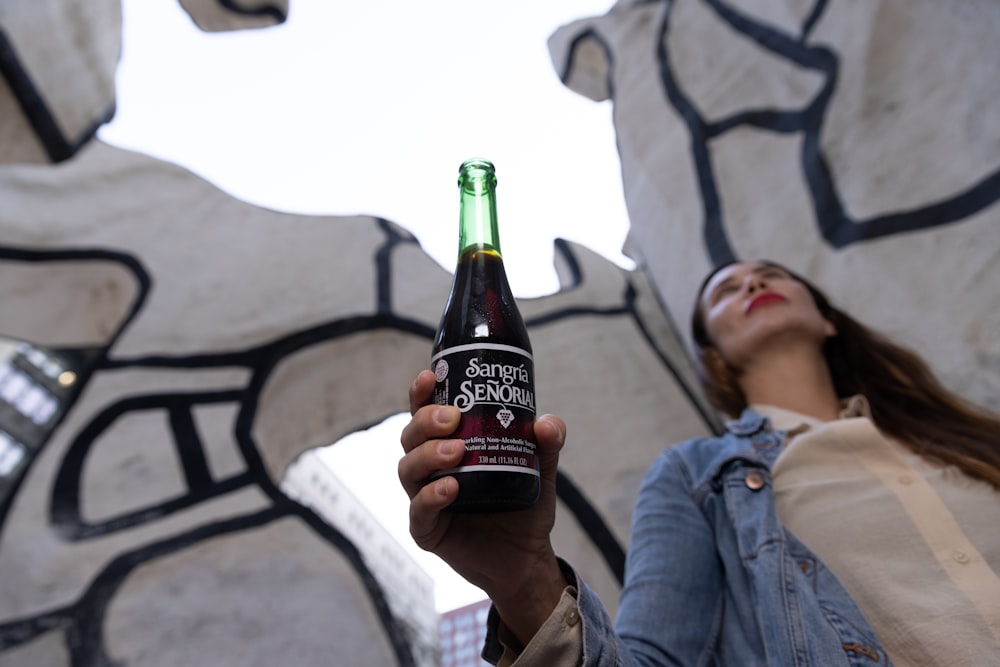 Hombre con chaqueta gris sosteniendo una botella negra