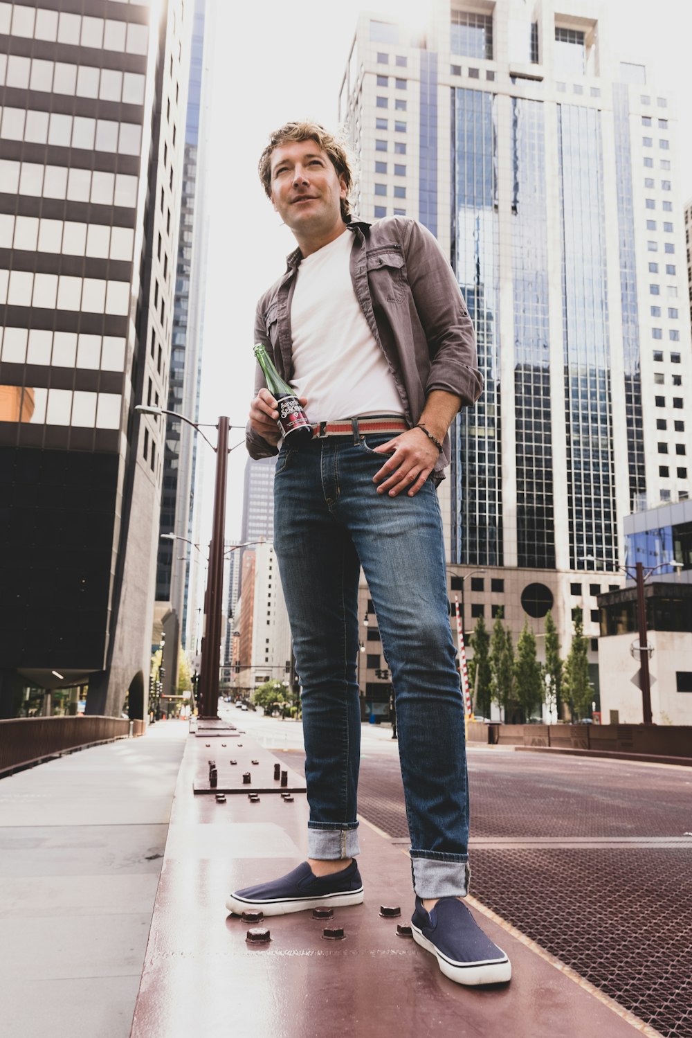 man in gray dress shirt and blue denim jeans standing on gray concrete pavement during daytime