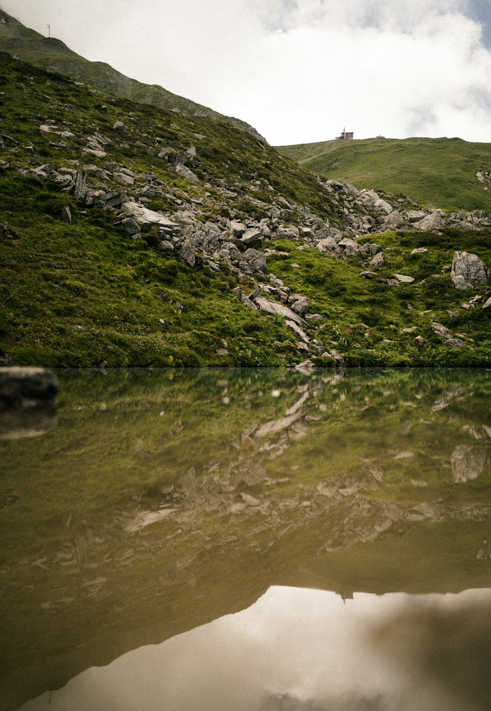 green grass covered mountain beside lake during daytime