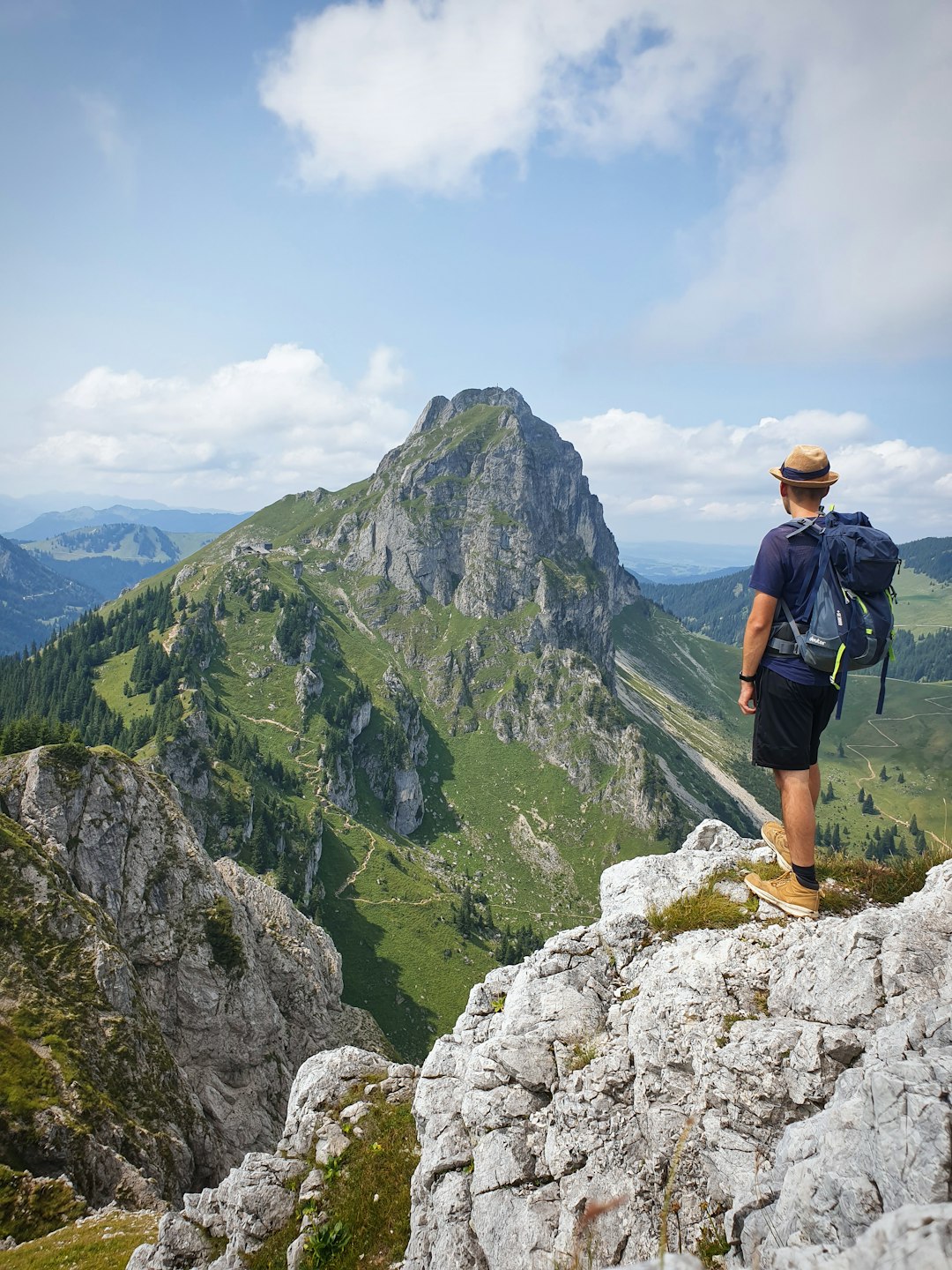 man in black shirt and blue denim shorts standing on rock mountain during daytime