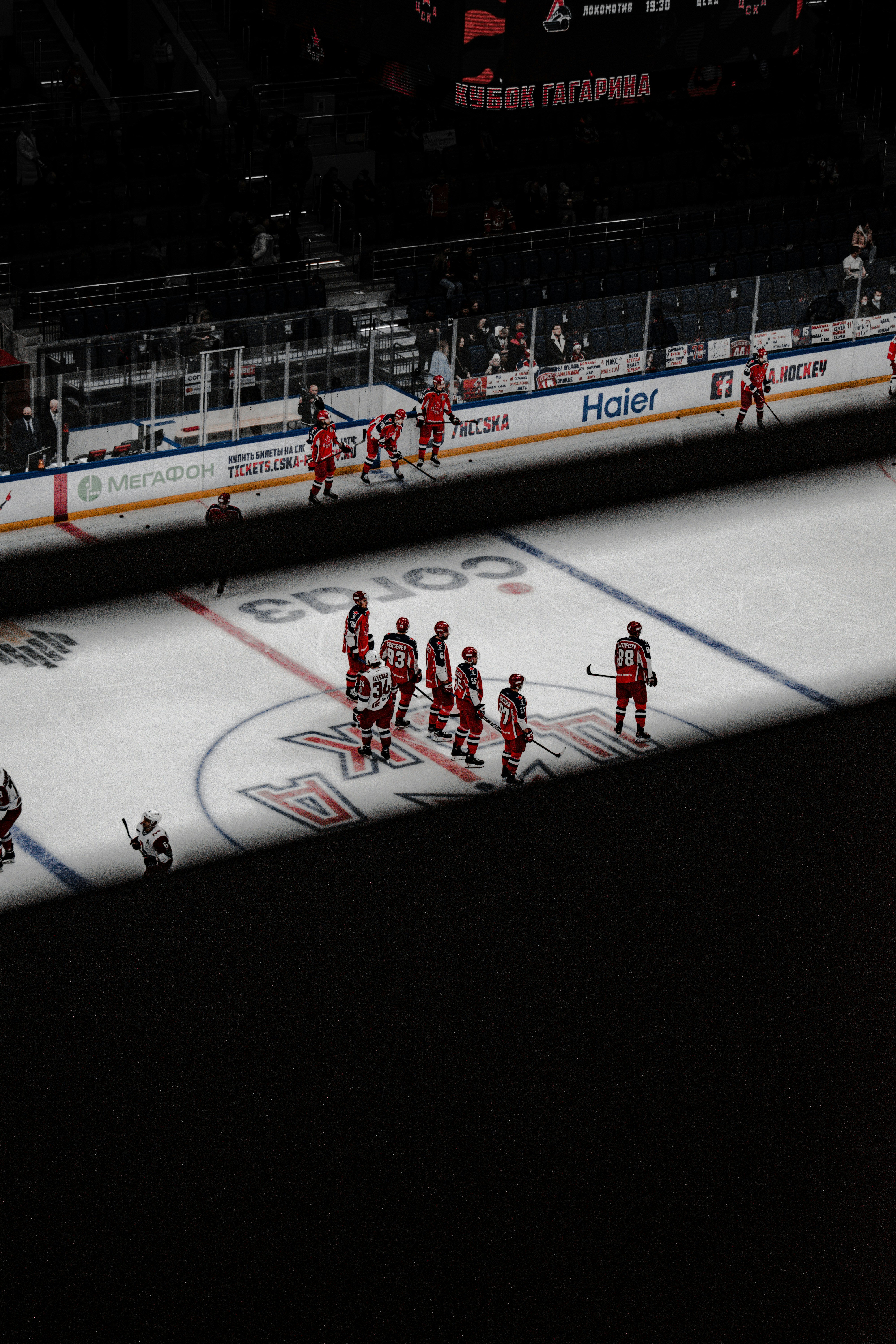 Hockey players celebrating goal on ice rink, dark arena with bright overhead spotlights, blue team jerseys