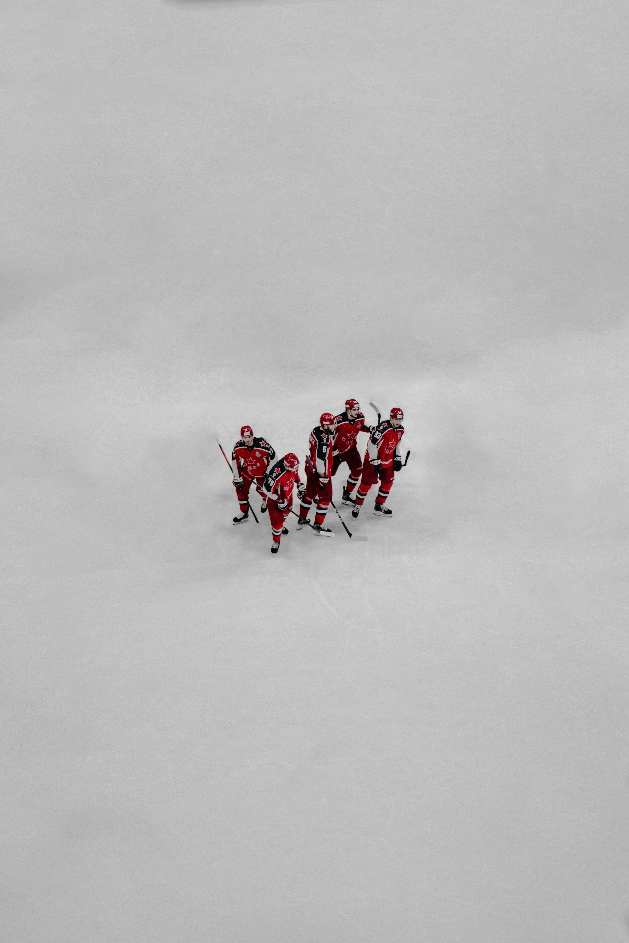 Menschen in roter Jacke und Hose spielen tagsüber Eishockey auf schneebedecktem Feld