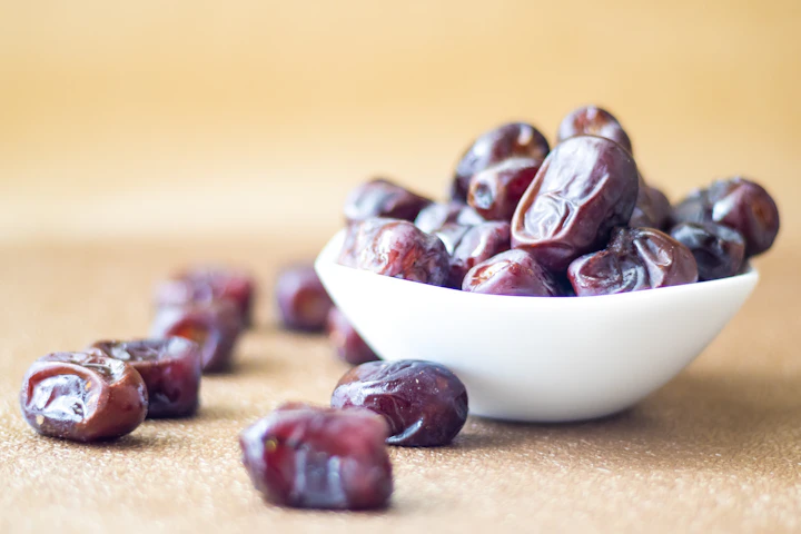Dates in a small white bowl with a few spilling onto the table
