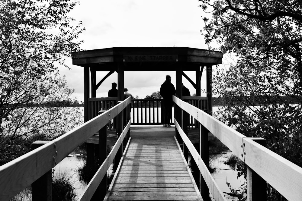 grayscale photo of woman walking on wooden bridge