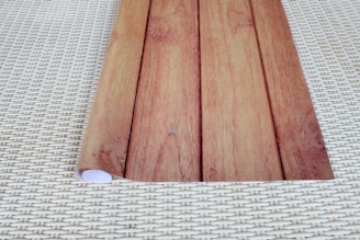 A piece of paper or material with a wooden pattern print is rolled partially on one side, placed on a surface with a woven pattern.
