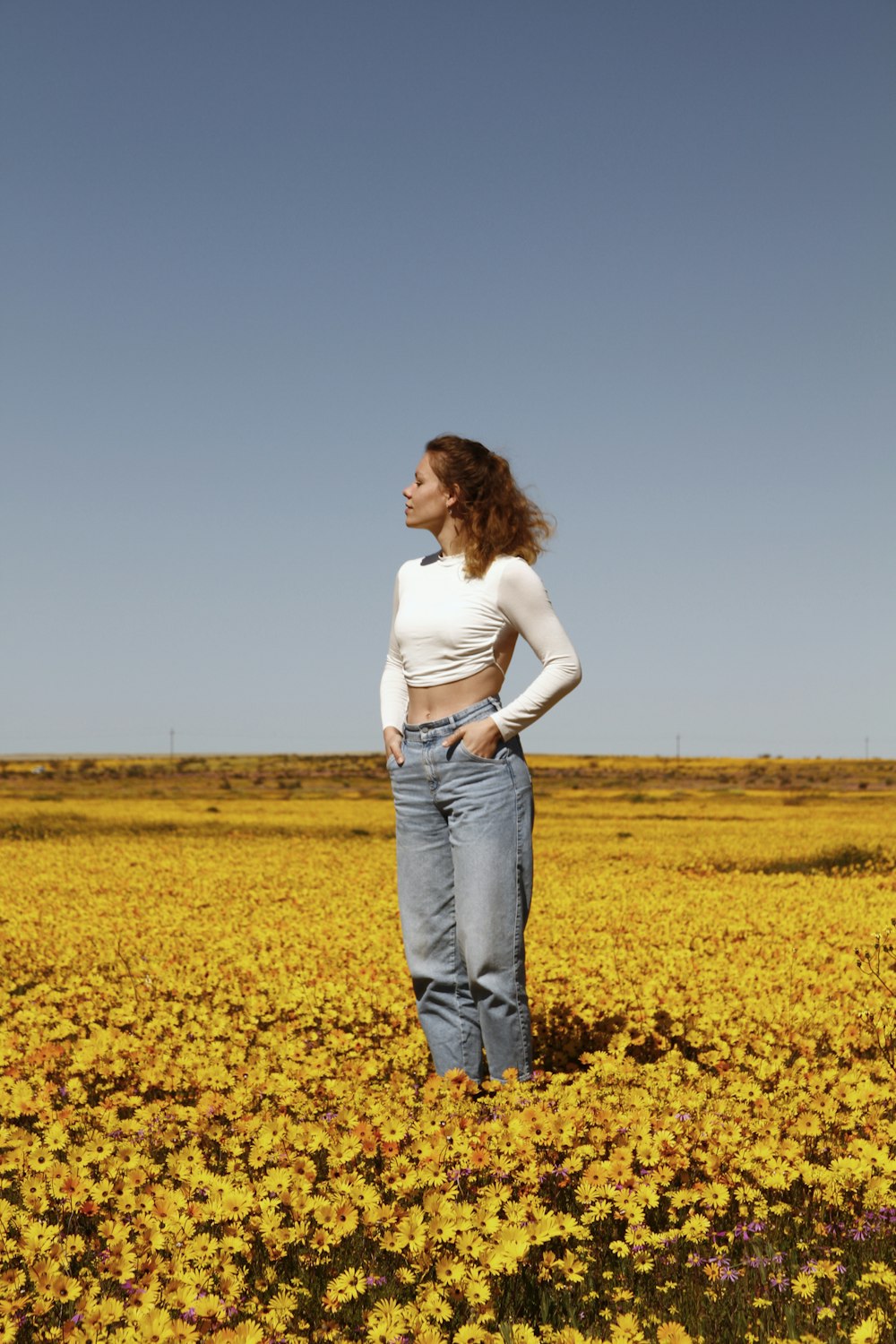 woman in white shirt and blue denim jeans standing on yellow flower field during daytime