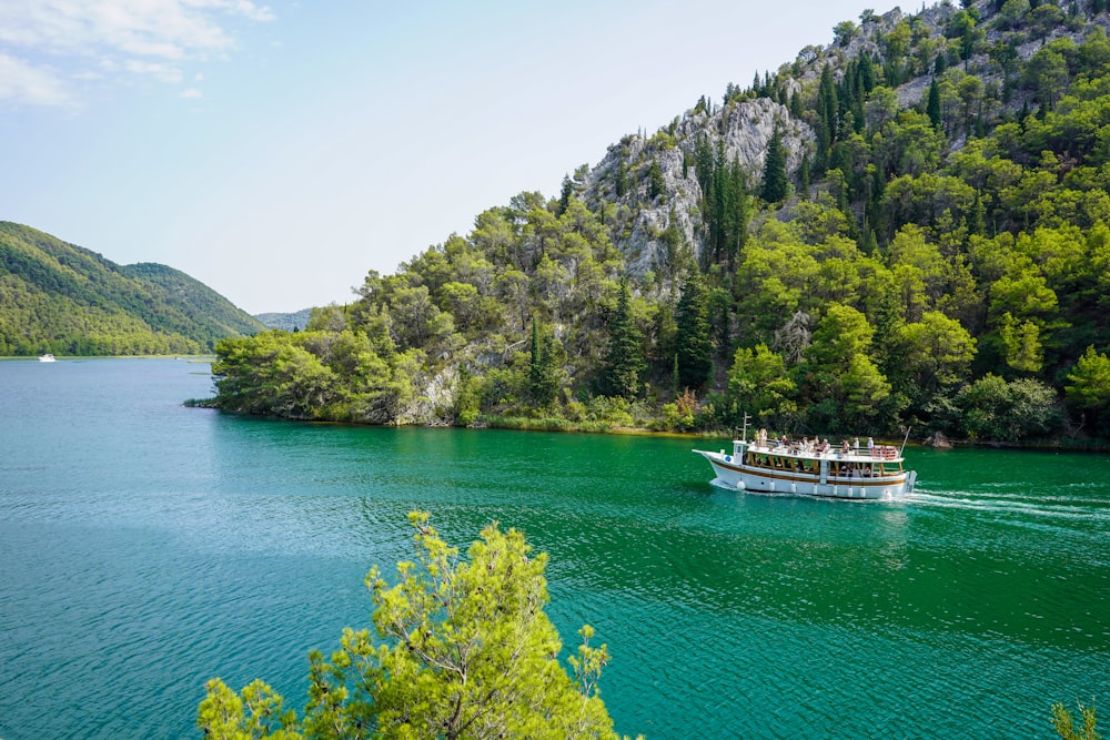 barca bianca sull'acqua blu del mare vicino agli alberi verdi e alla montagna durante il giorno