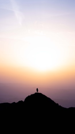 A powerful silhouette of a person standing tall on a mountain peak at sunrise.