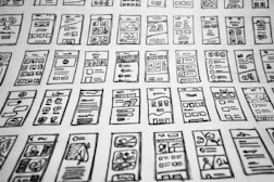 Multiple hand-drawn sketches of mobile user interface designs are spread out in a grid pattern. Each sketch contains various UI elements such as buttons, text boxes, images, and icons.