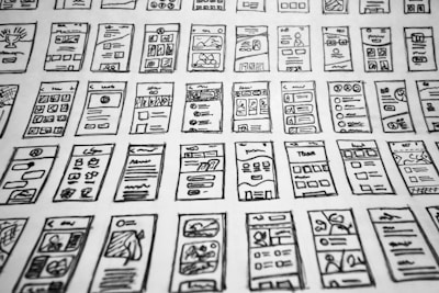 Multiple hand-drawn sketches of mobile user interface designs are spread out in a grid pattern. Each sketch contains various UI elements such as buttons, text boxes, images, and icons.