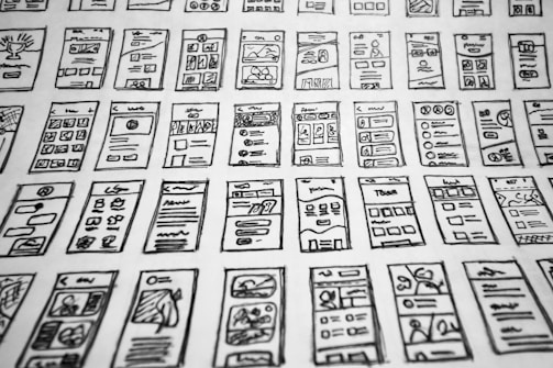 Multiple hand-drawn sketches of mobile user interface designs are spread out in a grid pattern. Each sketch contains various UI elements such as buttons, text boxes, images, and icons.