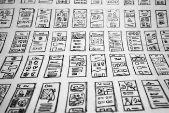 Multiple hand-drawn sketches of mobile user interface designs are spread out in a grid pattern. Each sketch contains various UI elements such as buttons, text boxes, images, and icons.