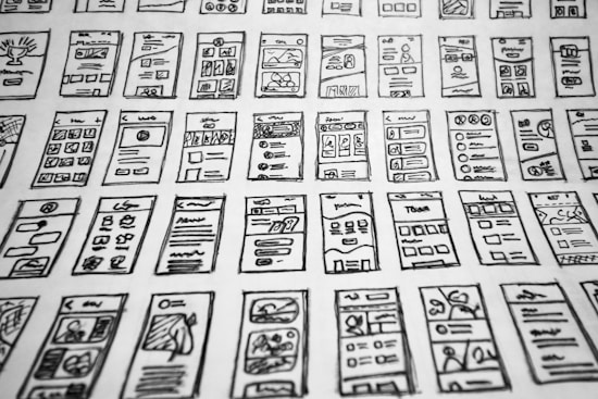Multiple hand-drawn sketches of mobile user interface designs are spread out in a grid pattern. Each sketch contains various UI elements such as buttons, text boxes, images, and icons.