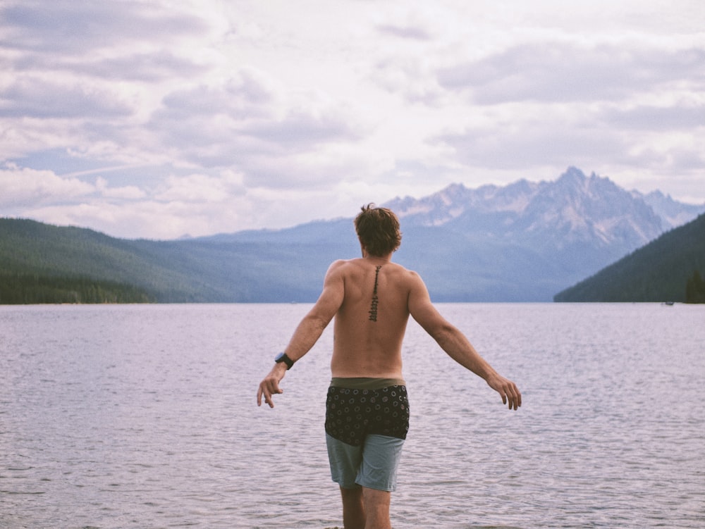 topless boy in black shorts standing on brown wooden dock during daytime