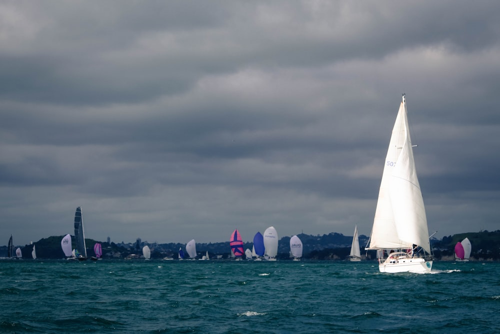 white sail boat on sea under gray sky