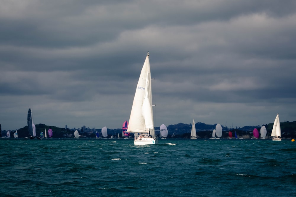 white sail boat on sea under gray sky