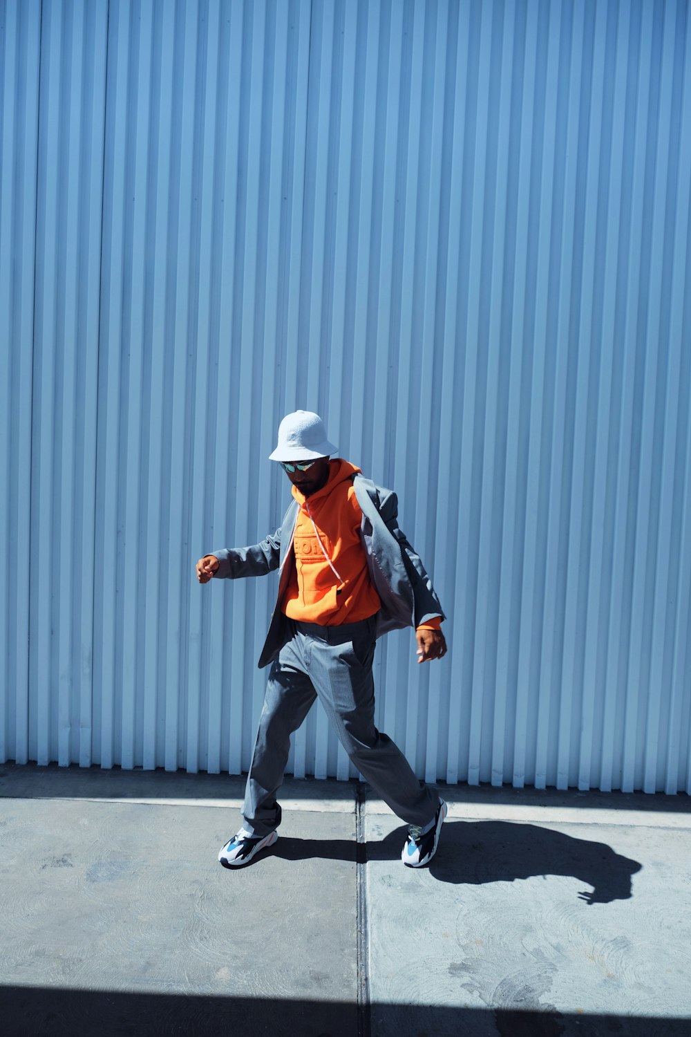 man in black jacket and black pants wearing white hat walking on sidewalk during daytime