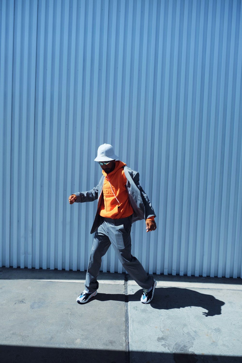Hombre con chaqueta negra y pantalones negros con sombrero blanco caminando en la acera durante el día