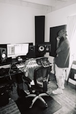 man in gray jacket and white pants standing beside black speaker