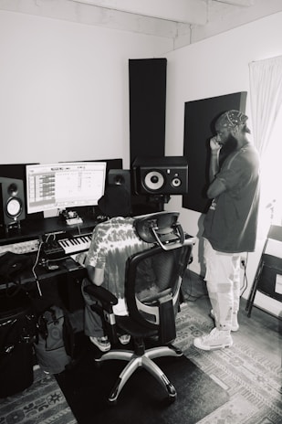 man in gray jacket and white pants standing beside black speaker