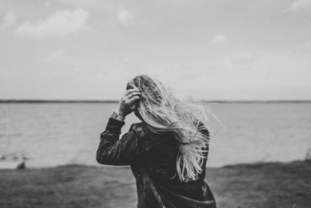 grayscale photo of woman in black jacket standing near body of water