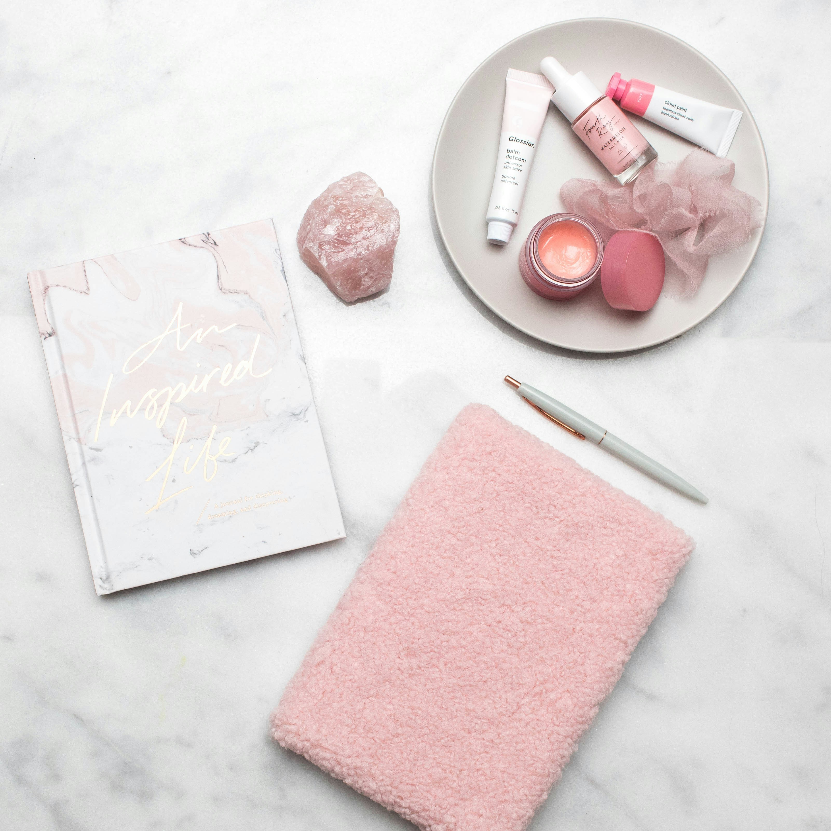 Beauty and skincare products arranged on pink marble surface, soft pastel lighting