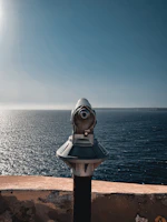 gray and black telescope on brown concrete surface near body of water during daytime