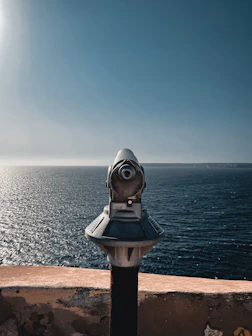 gray and black telescope on brown concrete surface near body of water during daytime