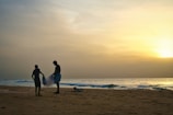 man and woman walking on beach during sunset